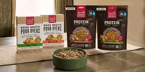 Two boxes of dog food broth and two bags of protein dog food toppers sitting on a kitchen table