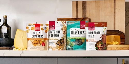 4 bags of The Honest Kitchen Dog Treats sitting on a kitchen counter with orange biscuits and cheese