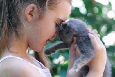 A young girl gently touching noses with a gray kitten, outdoors.