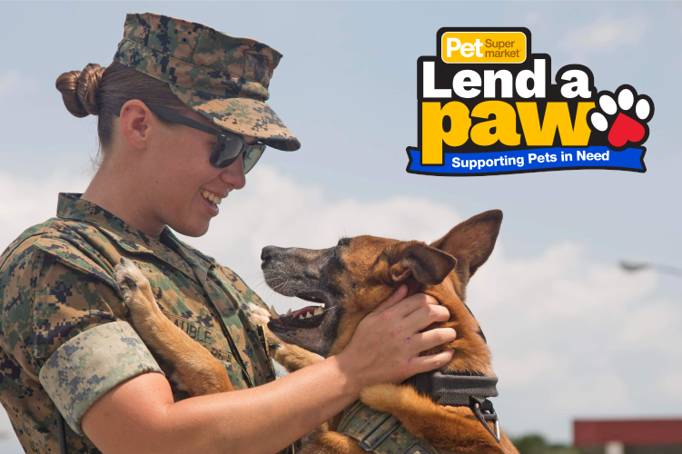 A soldier in uniform smiling and holding a Belgian Malinois with the text "Pet Supermarket Lend a Paw - Supporting Pets in Need" in the background.