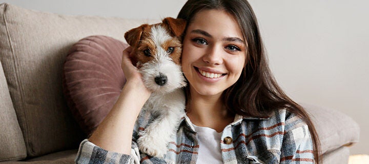 A young woman smiling and cuddling with a small dog on a couch, highlighting their close bond.