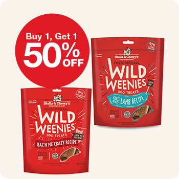 Two red packs of Stella & Chewy’s Wild Weenies dog treats in "Bacon Me Crazy" and "Grass-Fed Lamb" recipes, with a red circular label reading "Buy 1, Get 1 50% OFF".